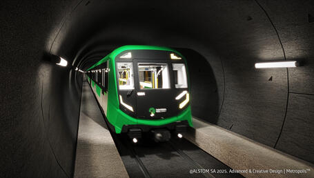 The image shows a modern metro train travelling through a dark tunnel, lit by longitudinal lights fixed to the walls. The train, with its resolutely contemporary design, has a green and black livery. The sleek, angular front incorporates white LED lighting in the form of sharp lines, with the words “Suburban Rail Loop” in white lettering. Through the large windows in the cab and cars, you can see the train’s bright interior.