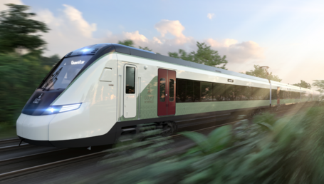 L’image montre un train moderne filant à vive allure sur une voie ferrée entourée de végétation luxuriante. Au premier plan, le train occupe la majorité de l’image : sa forme aérodynamique et ses lignes épurées évoquent une conception contemporaine. La motrice présente une face avant arrondie, soulignée par des éclairages LED bleu clair qui renforcent son aspect technologique. Sur le côté, la livrée combine des tons blancs, gris et verts.
